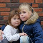 two little girls hugging each other in front of a brick wall